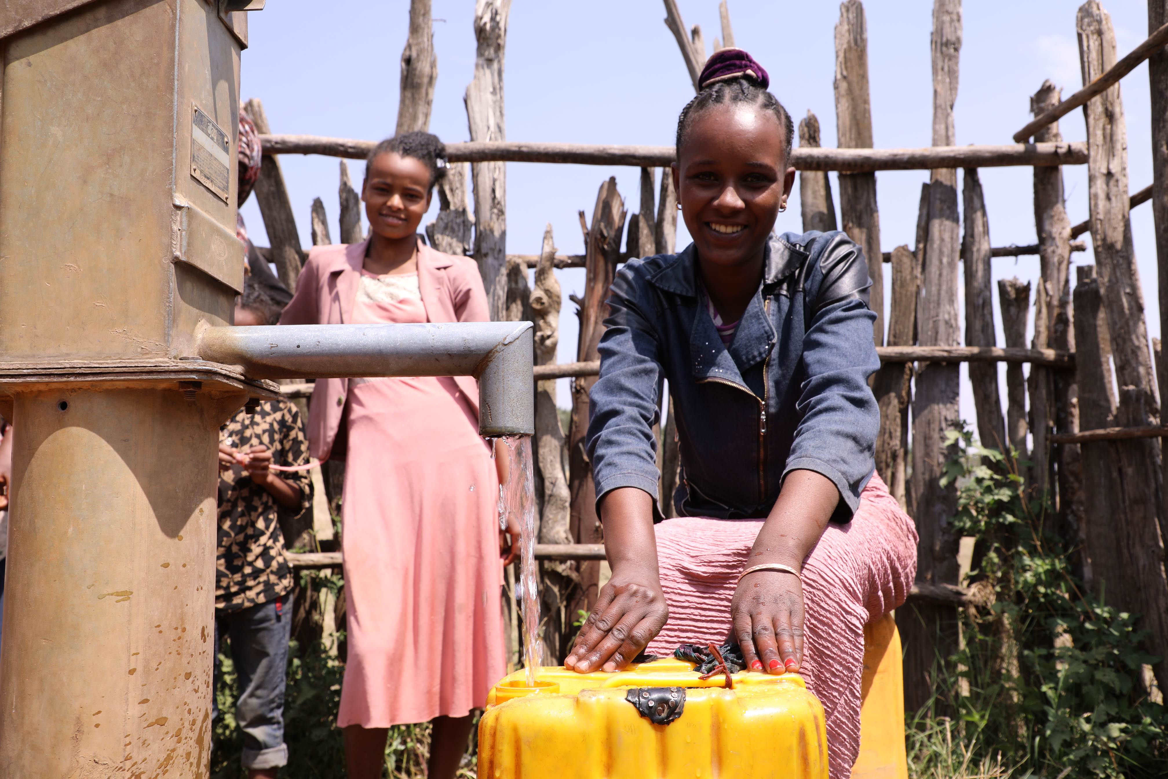 Girl from Ethiopia pours water from public tap into a yellow tub to take home
