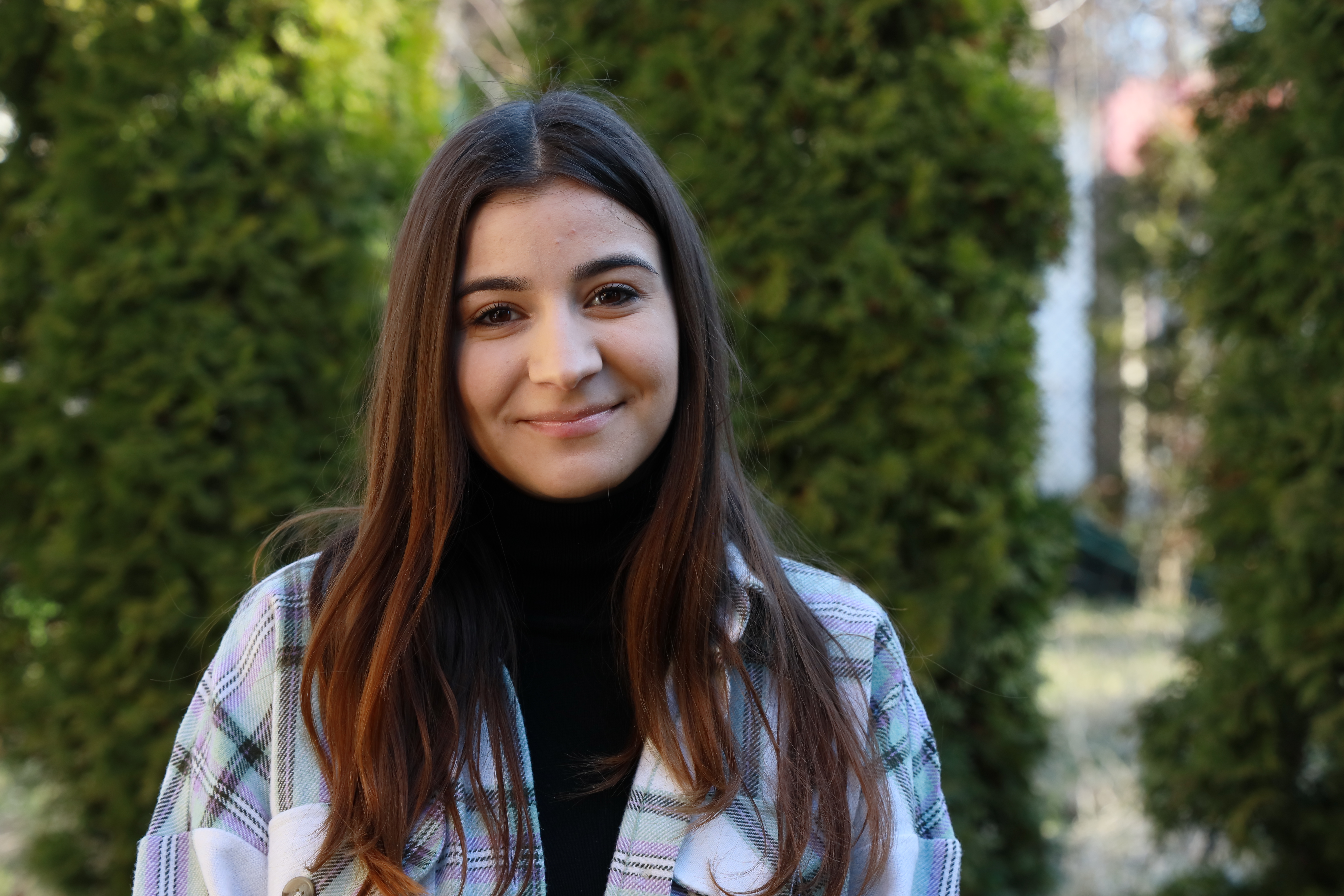 A 21-year old girl from Romania smiling and looking directly into the camera in a park