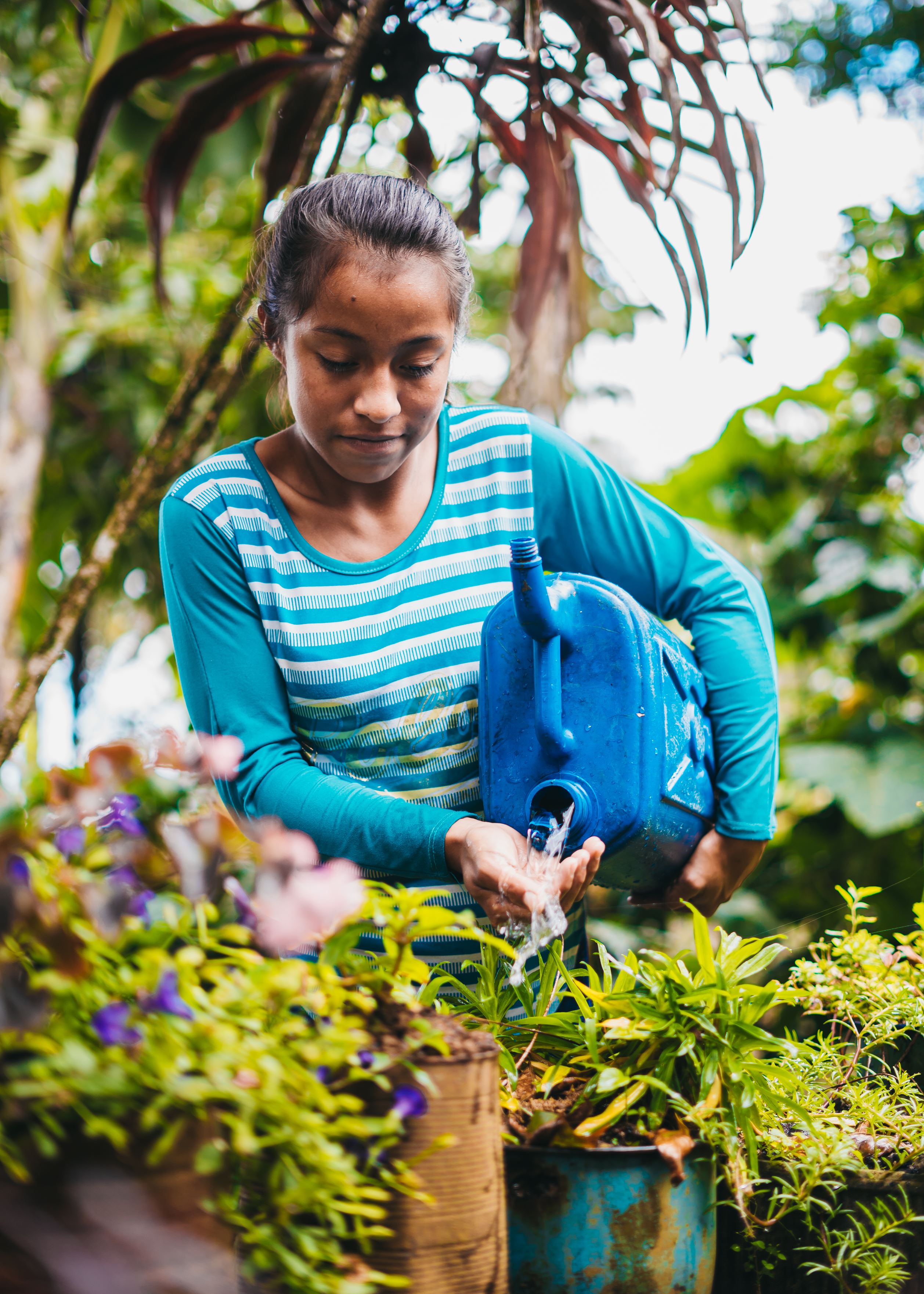 Girl from Honduras watering her plants with a blue water tub
