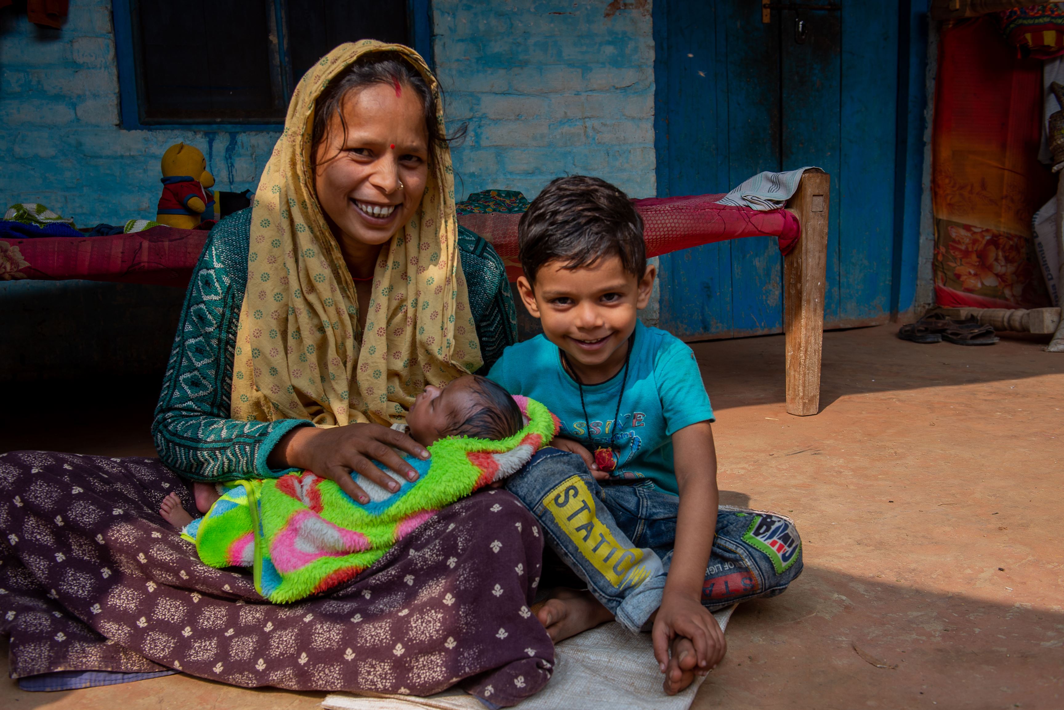 Mother from India and her son sitting on the floor in their house and smiling at the camera