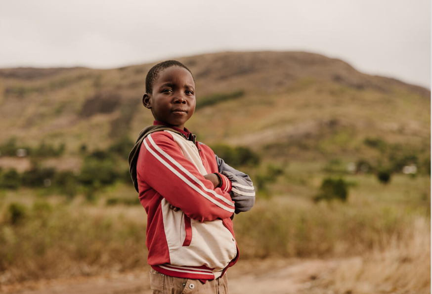 Boy from Malawi standing with his arms crossed in a field, looking at the camera
