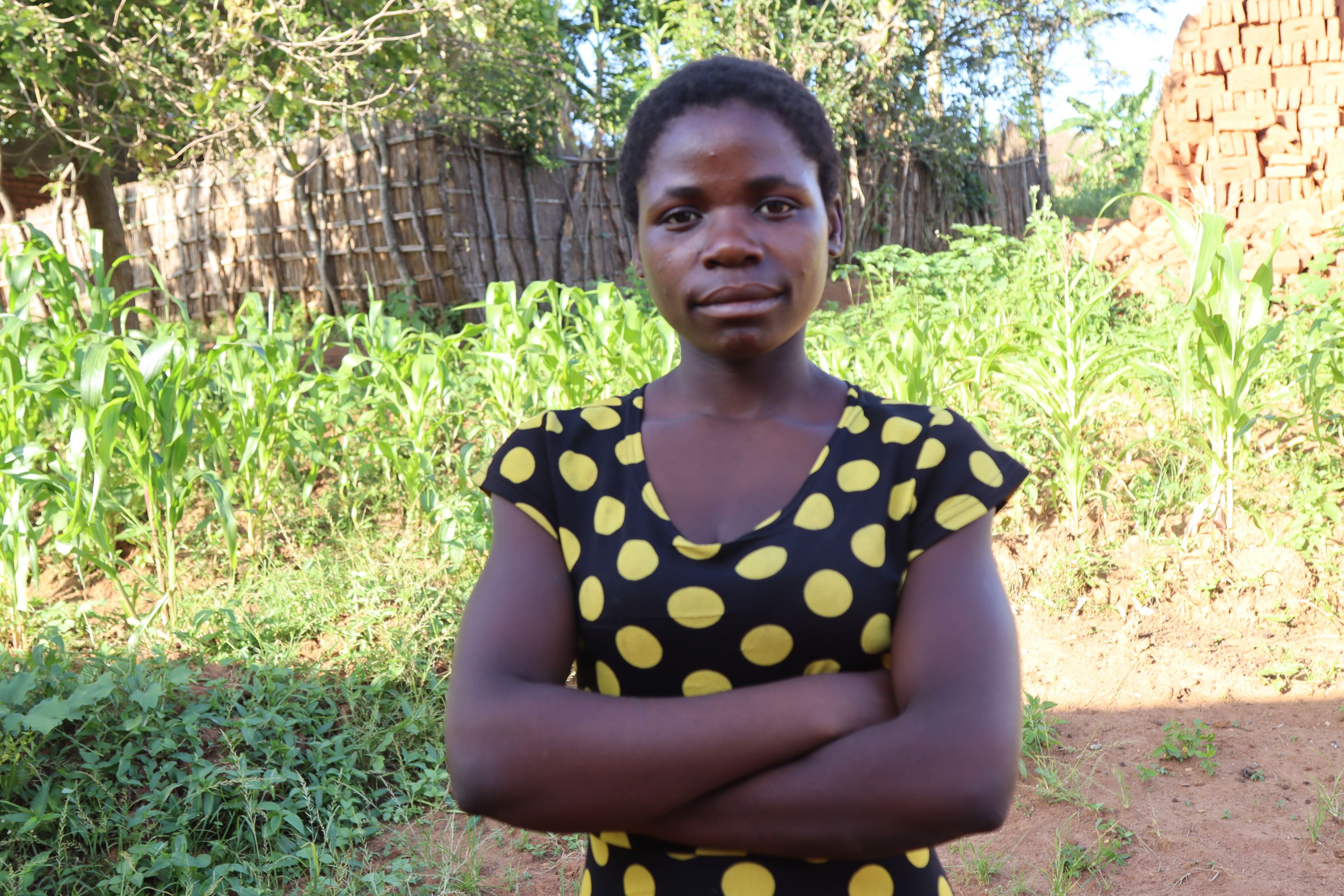 Girl from Malawi standing with her arms crossed in a field, looking at the camera