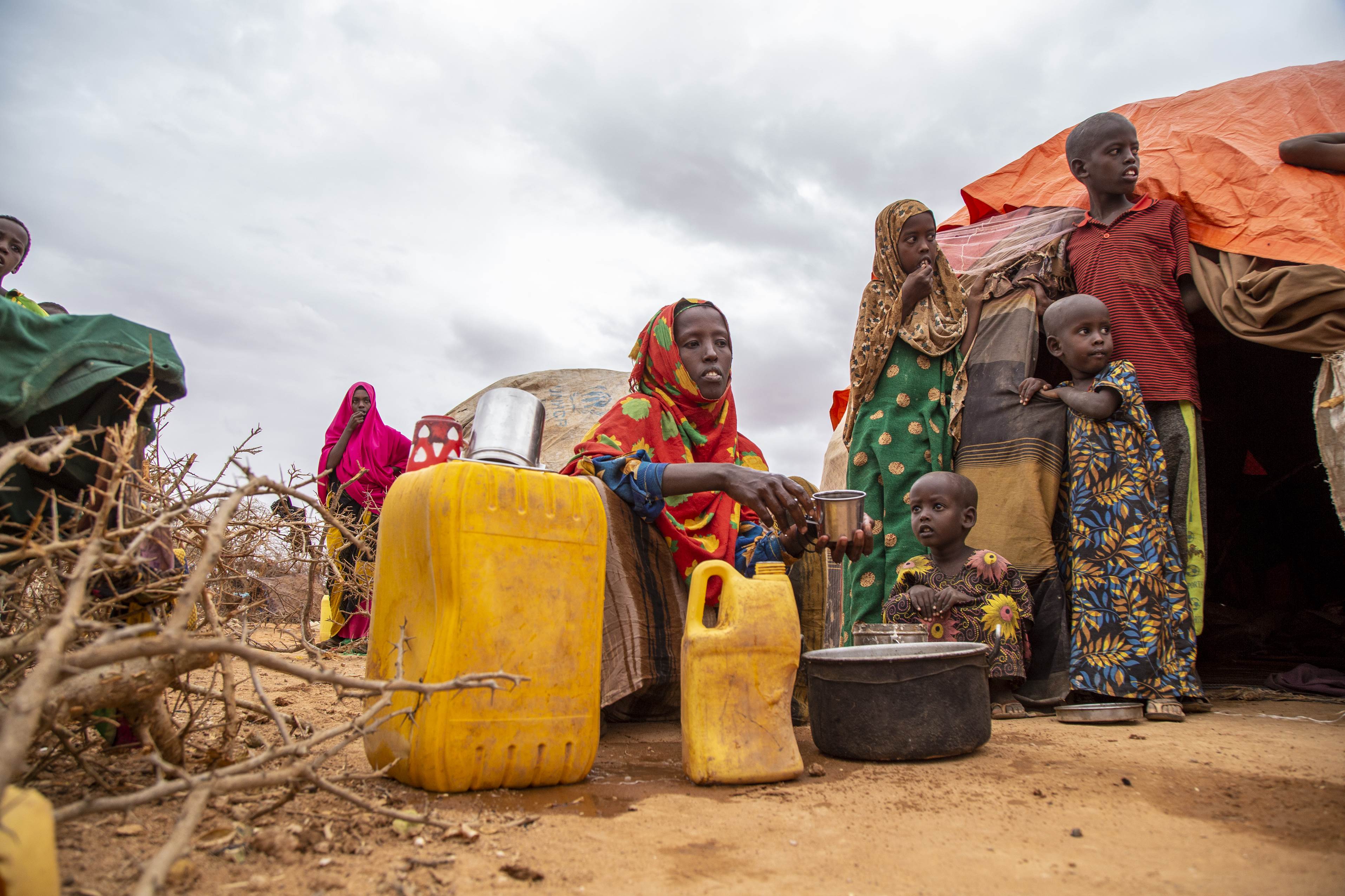 Widow in Somalia sitting between two yellow tubs of water delivered by World Vision