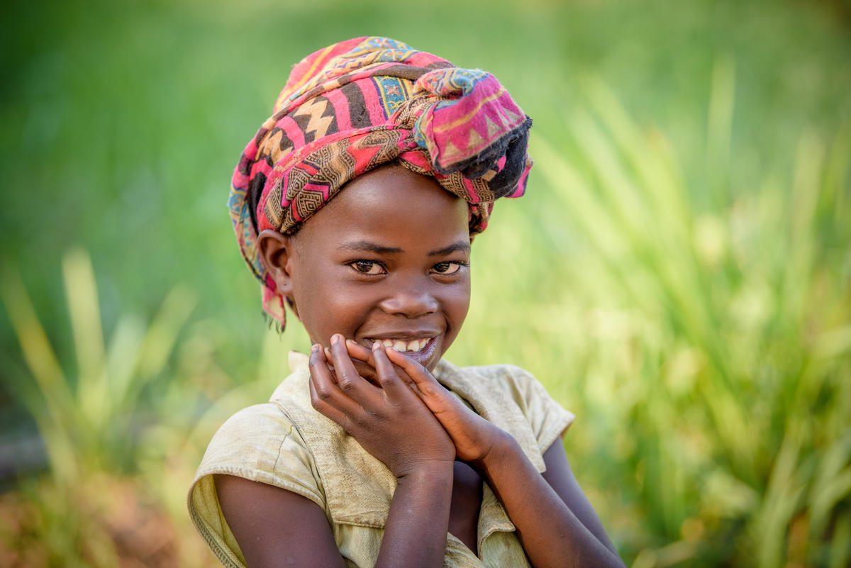 Girl in DRC smiles to camera wearing colourful head wrap