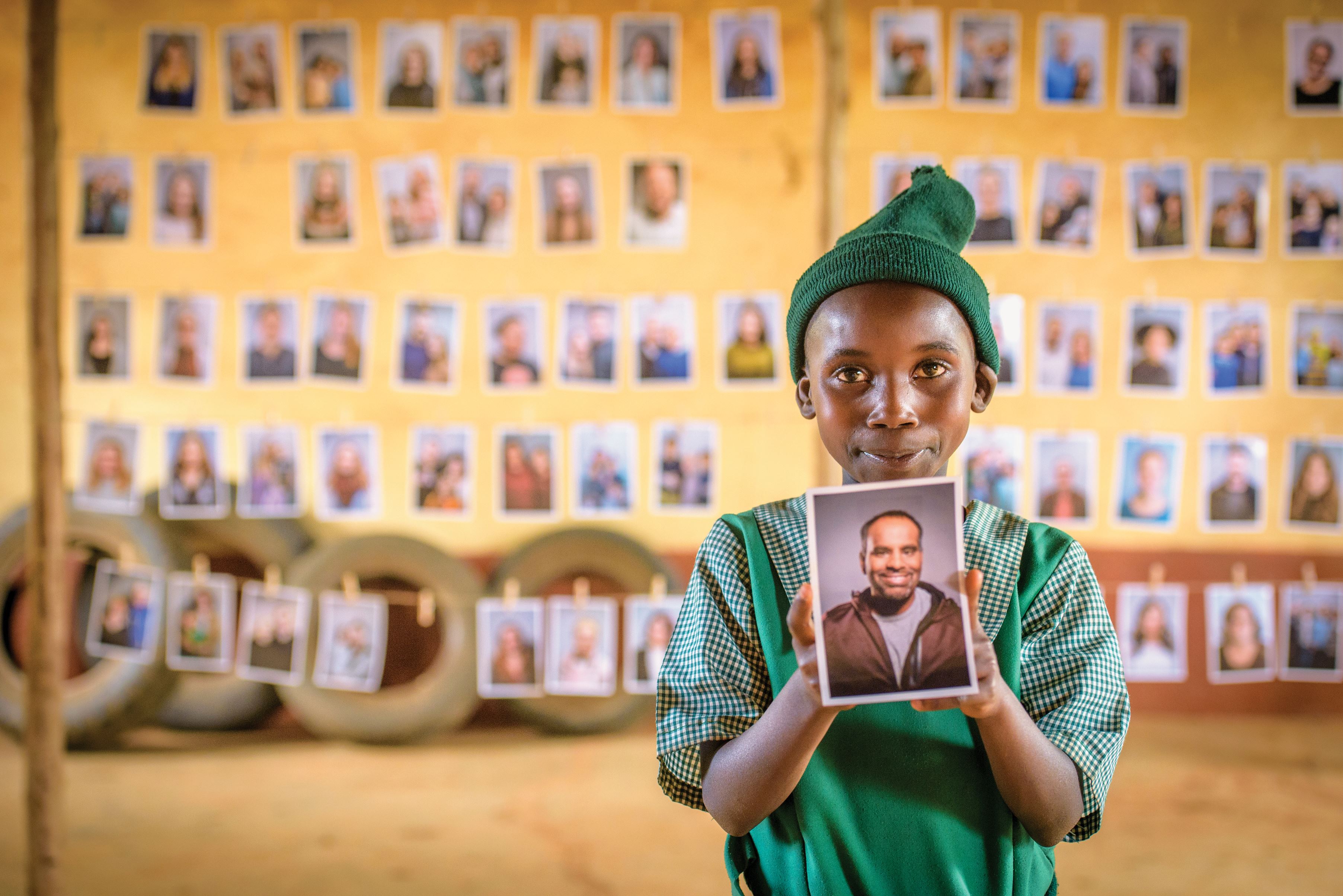 Young girl smiles and holds up photo of sponsors she has chosen