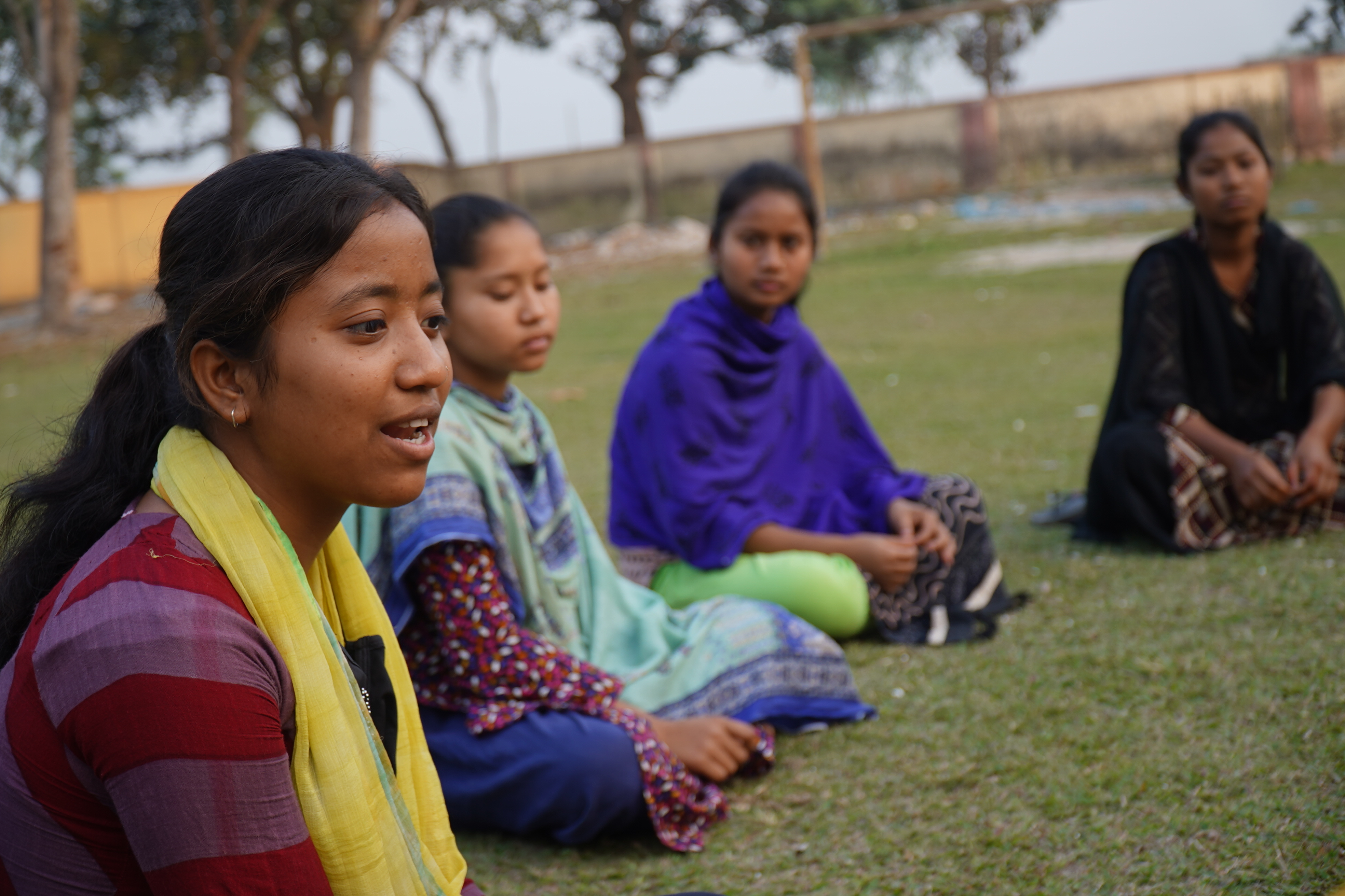 Sponsored girls from Bangladesh sitting closely in a circle in a field.