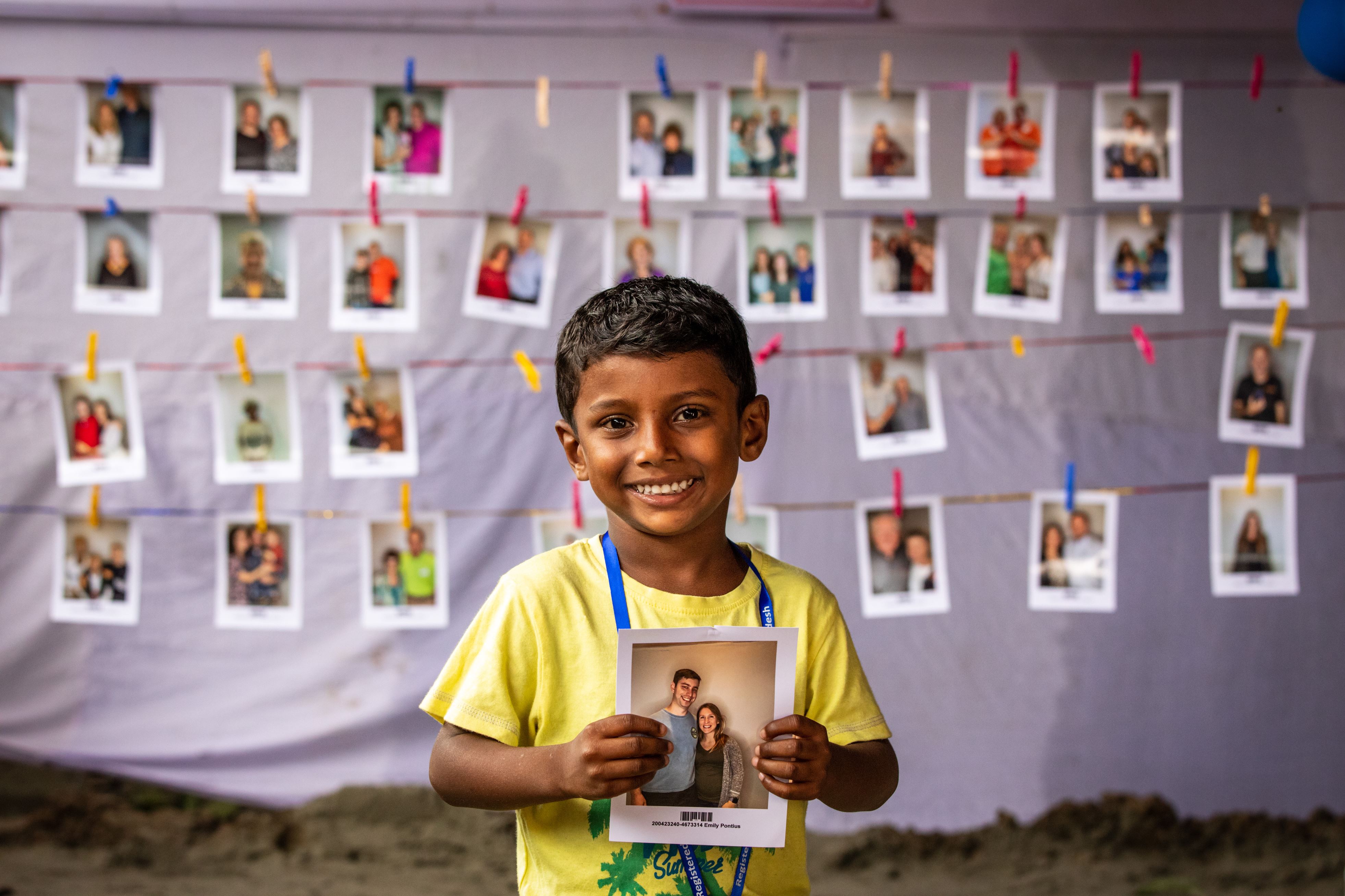 Boy from Bangladesh holding up his sponsor's photo and smiling