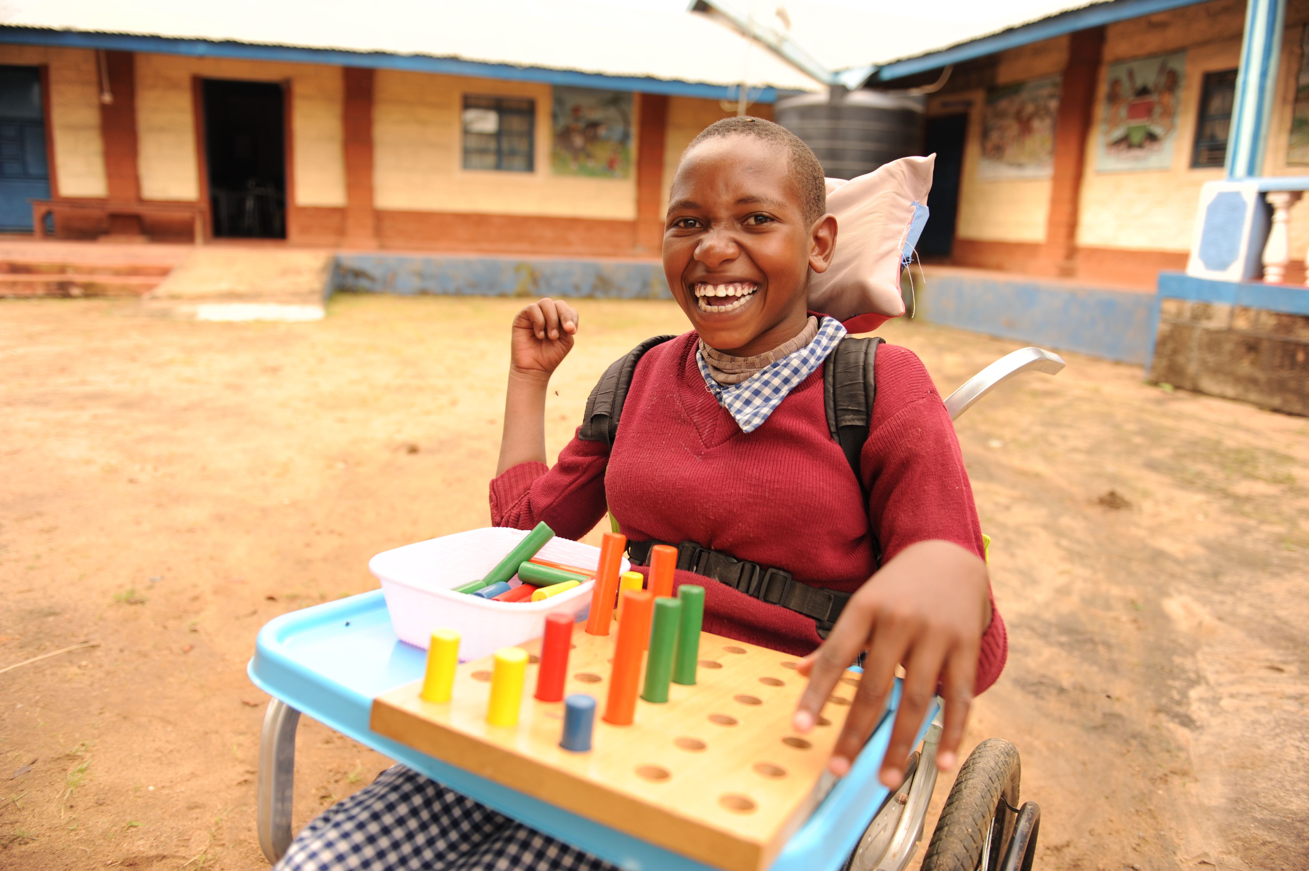 Girl from Kenya smiling while sitting in her wheelchair and playing with blocks