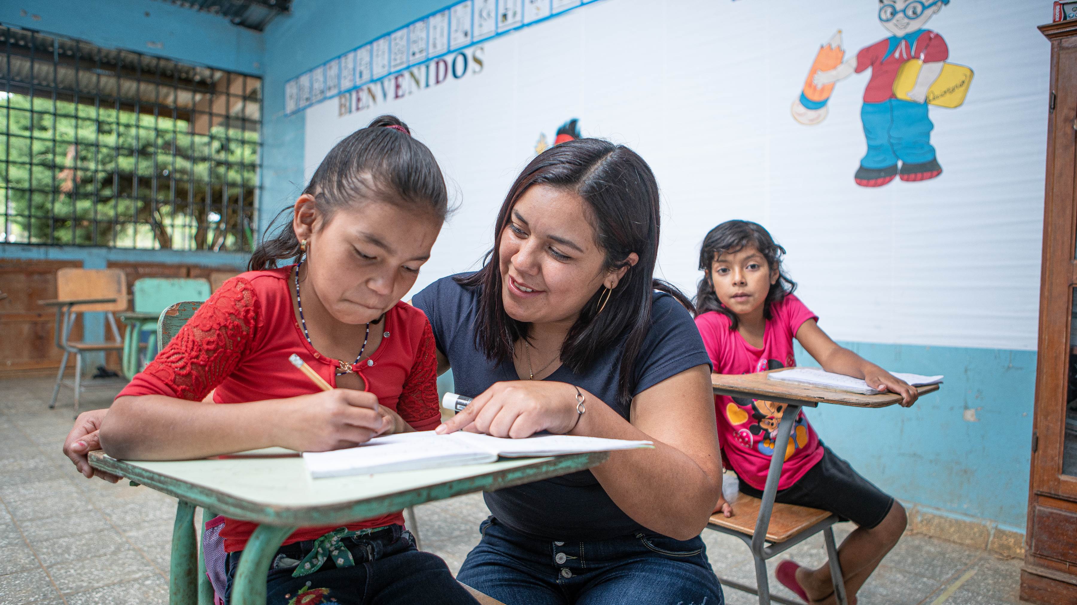 Teacher in Honduras helping a student with her work at her school desk