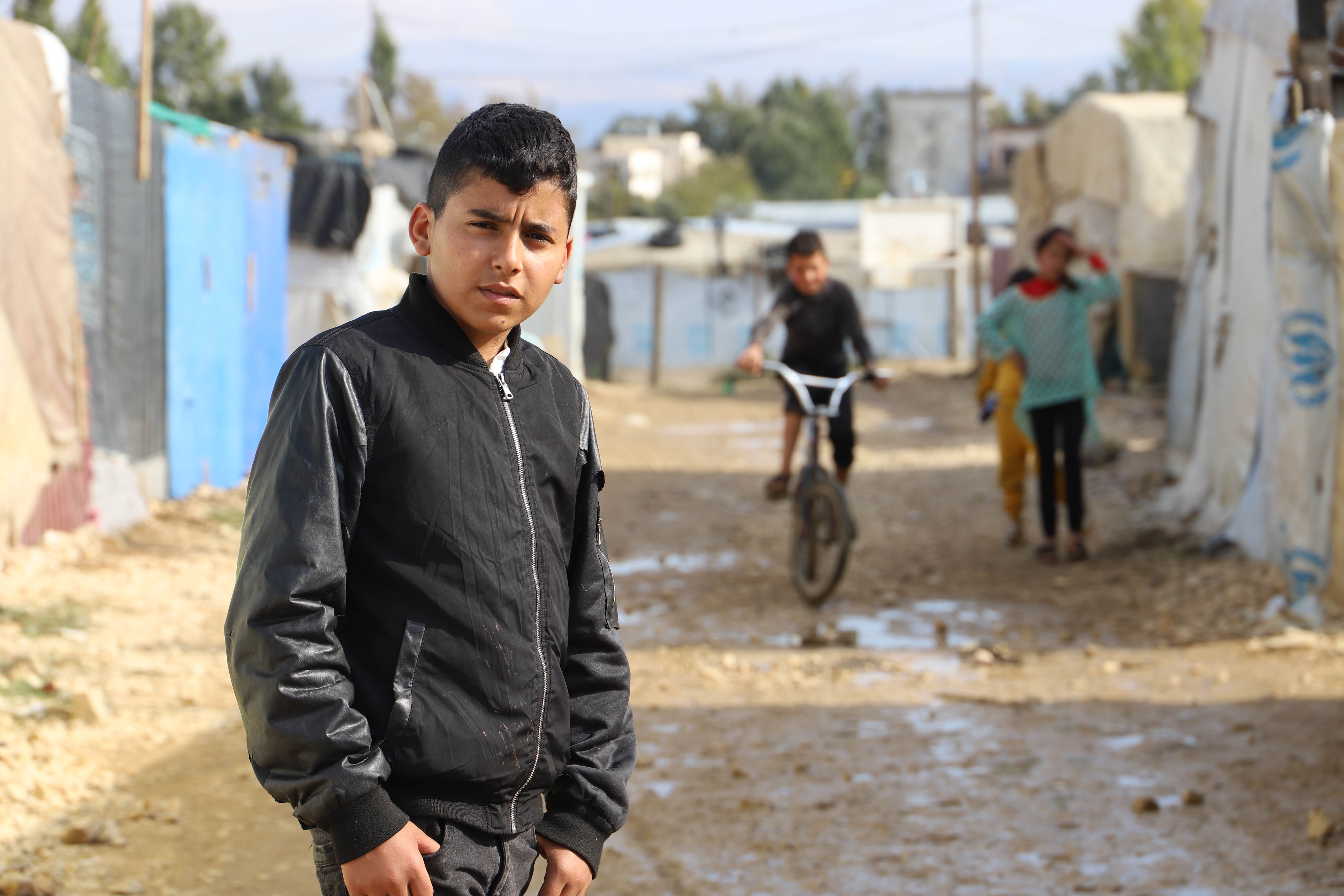 Syrian boy standing outside some tents in a refugee camp in Syria