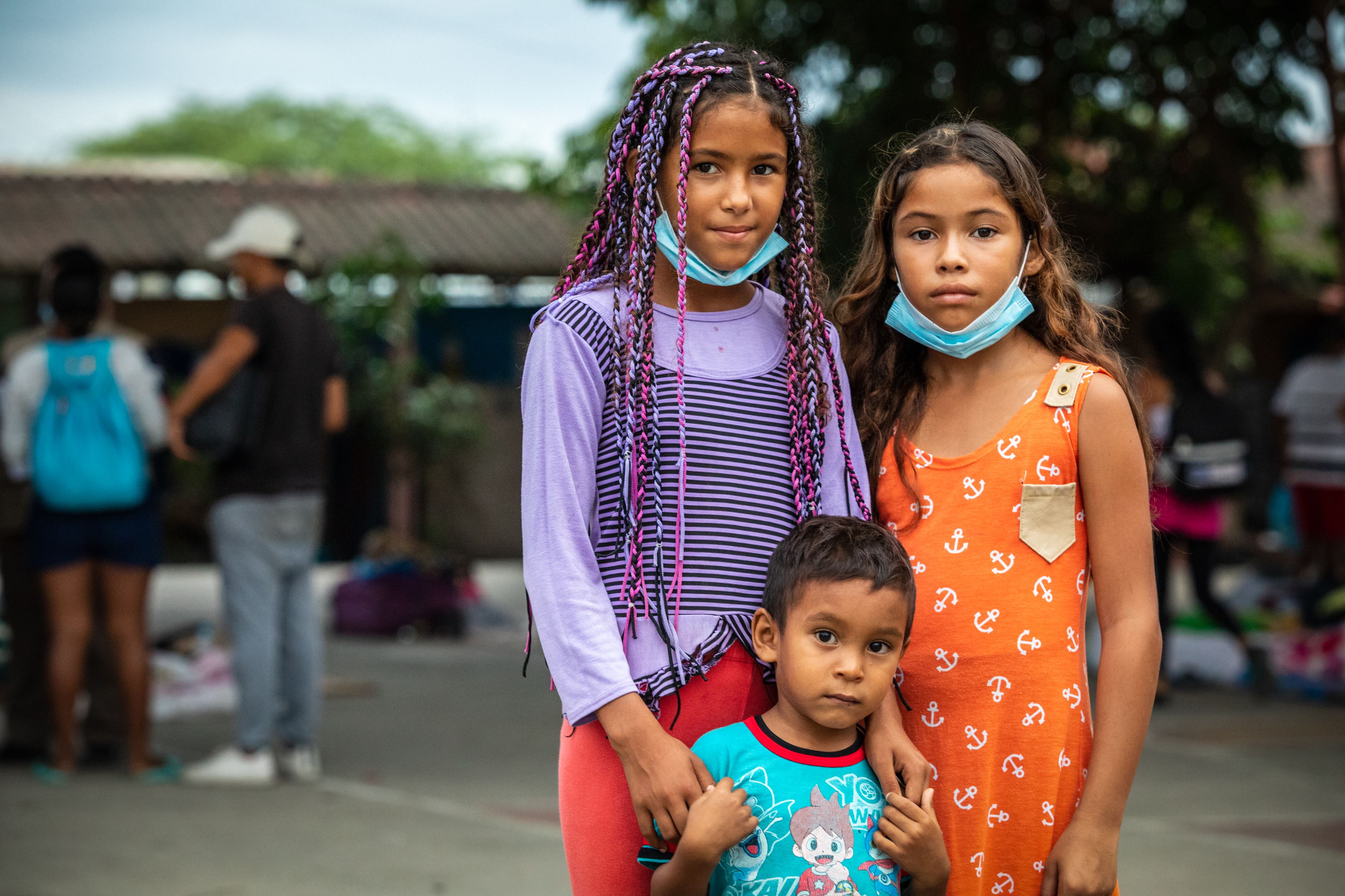 Three refugee children at the Peru-Ecuador border smiling and looking at the camera
