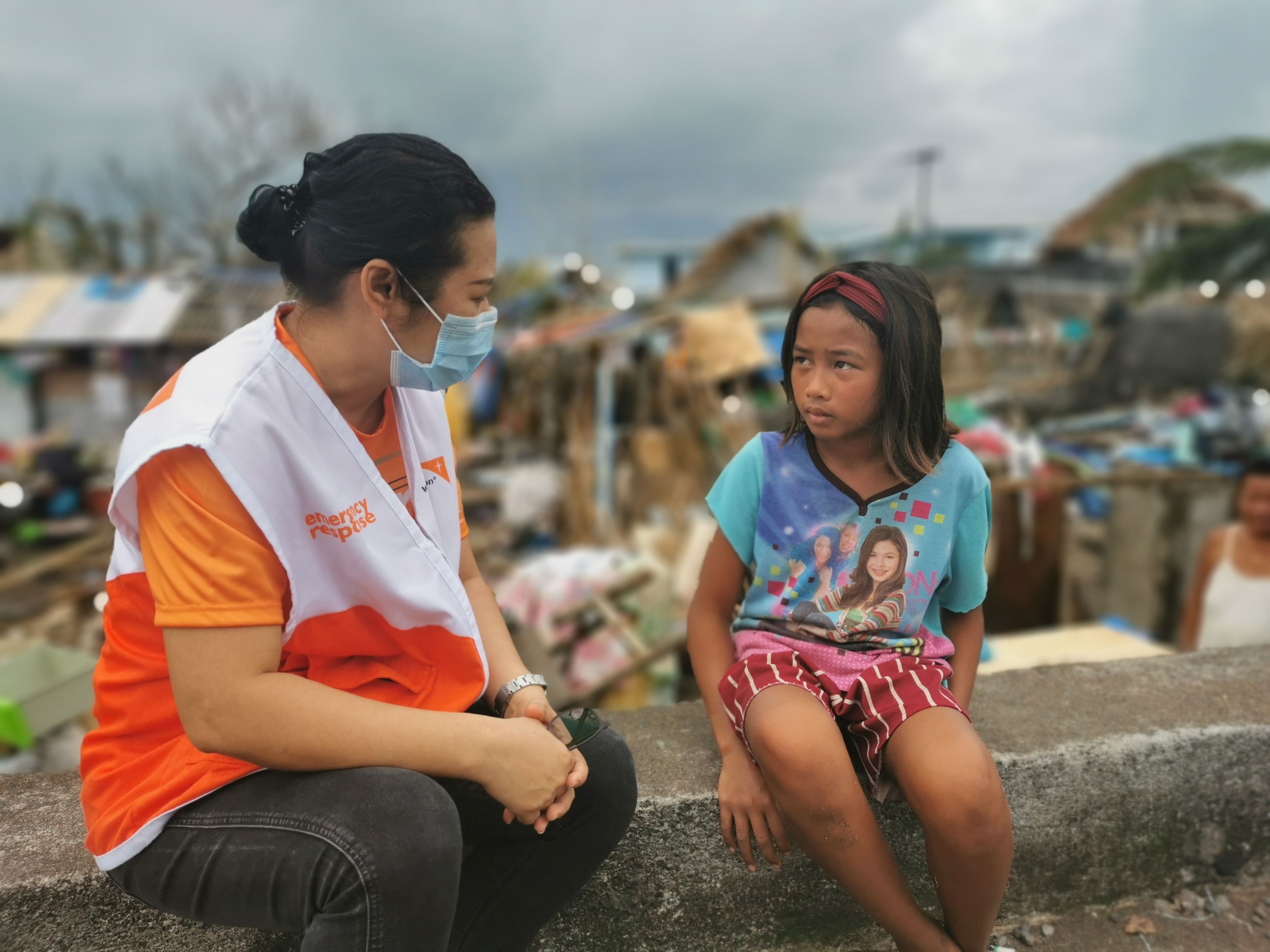 World Vision volunteer wearing a facemask talks to a girl from the Philippines