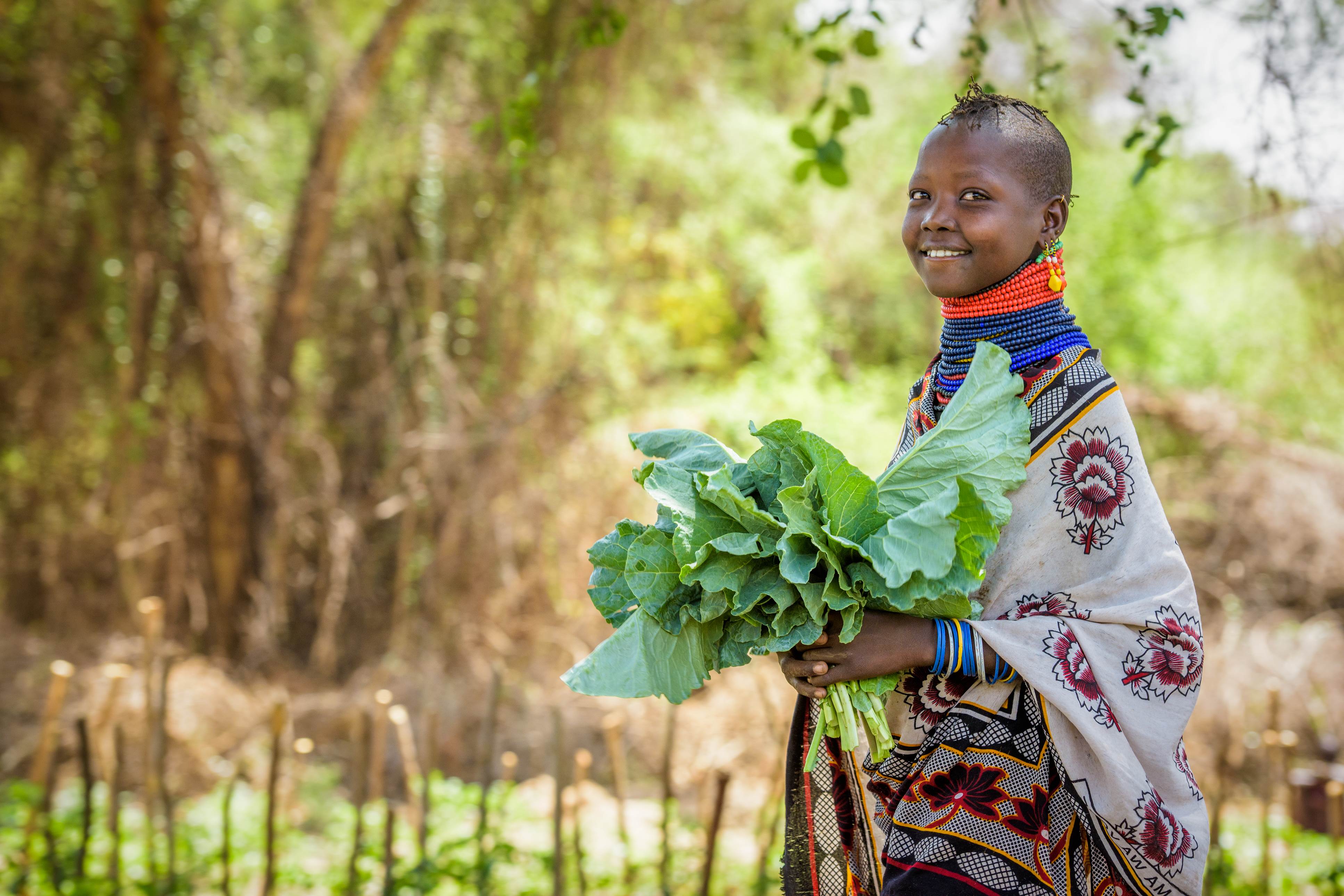 Girl in Kenya smiles as she stands in a field and holds lettuce