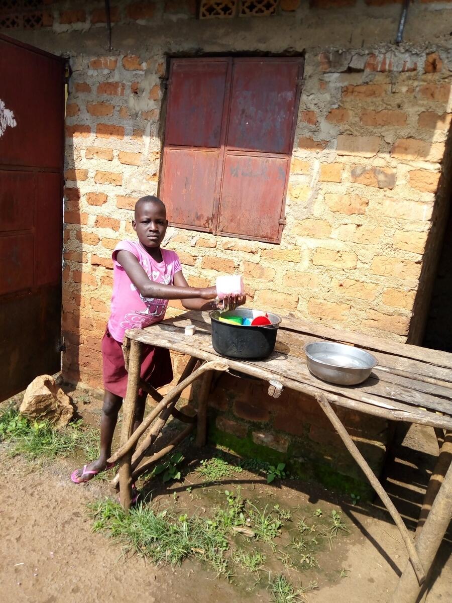 Judith in Uganda works outside in a pink shirt at home after a World Vision home-based class