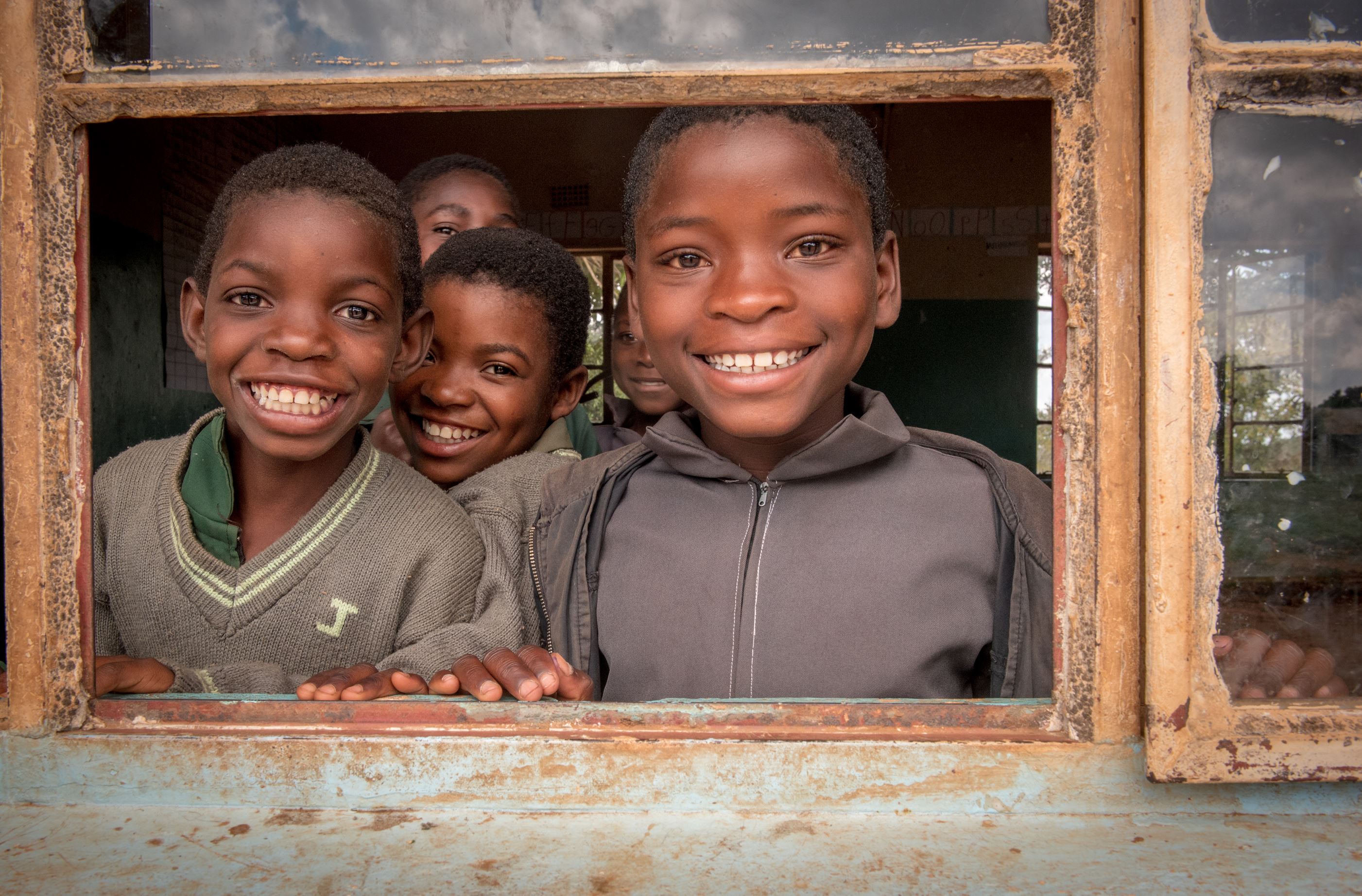 School children peering out of a window, smiling 