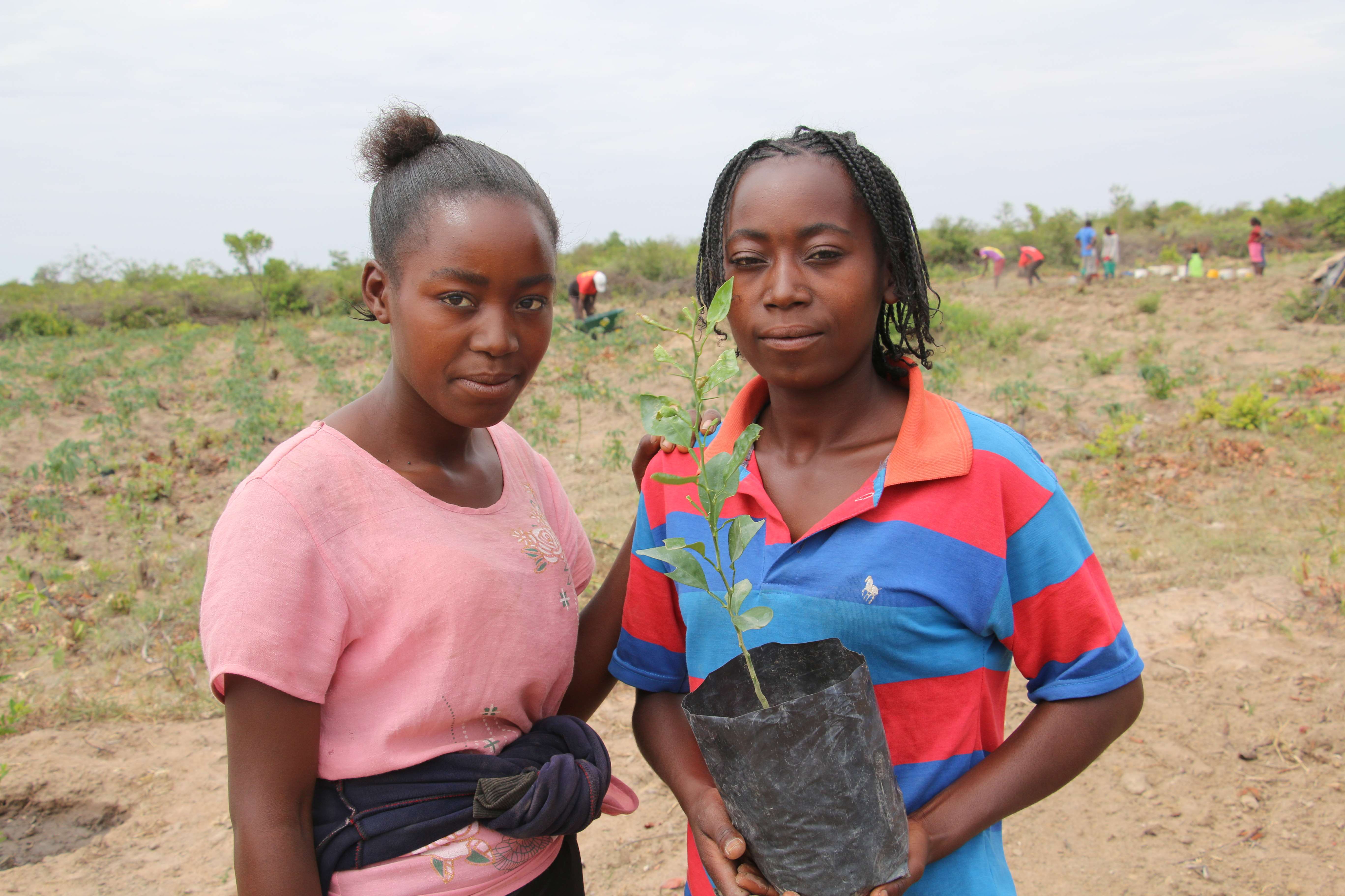 Sisters Julieta and Eularia holding up a plant pot with a crop they planted in their field farming school