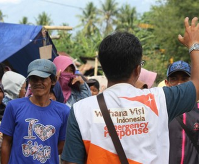 World Vision staff member waves with his back to camera in front of a crowd of people