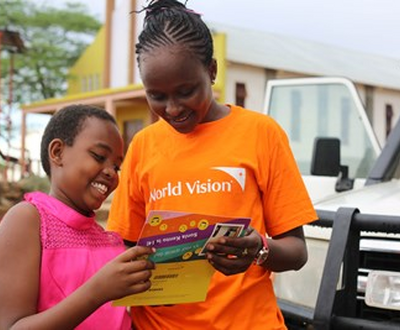 14 year old girl in Kenya, standing next to a World Vision worker, opens post from her sponsor