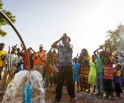 A community in Mali celebrates, dancing and raising arms skyward in front of a newly working borehole in Mali