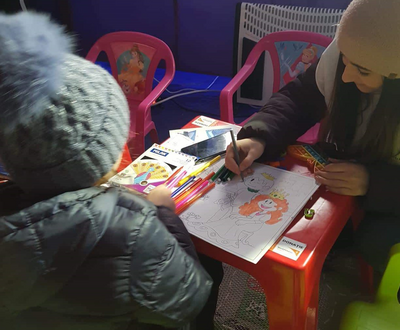 Woman painting with a girl at a camp.