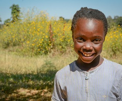 Former sponsored child smiles in field in Zambia