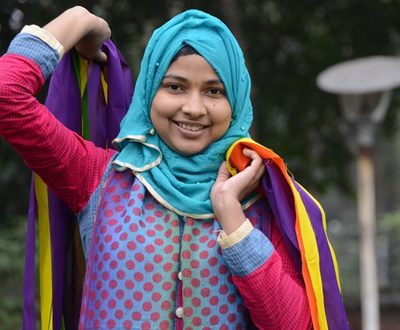 Young teenage girl in bright clothes holding material and smiling at the camera in Bangladesh
