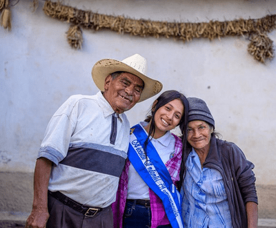 13 years old girl from Honduras is hugging her grandparents, wearing a blue sash signifying she is the youth mayor of her area