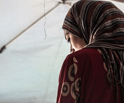 Child bride, Amai, now 13, from Iraq is seated with her headscarf wrapped tightly around her small face