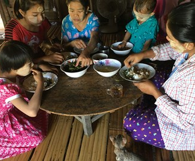A woman from Myanmar and four children sitting in a circle on the floor around their dinner table and eating with their hands