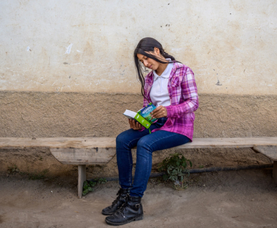 Nahomy sits outside on a bench, reading a favourite book