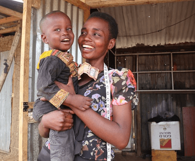 Mother in South Sudan is holding her young son and smiling at him as he smiles to the camera