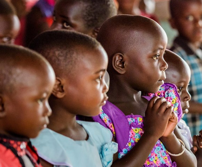 Ugandan children look off camera as they clasp hands together and pray