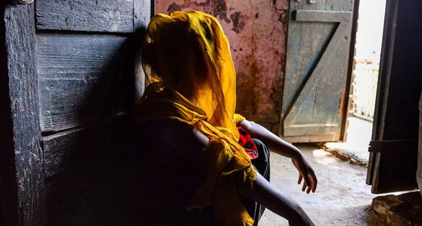 A girl looks away from the camera, her face covered in shadow as they recount her traumatic child marriage