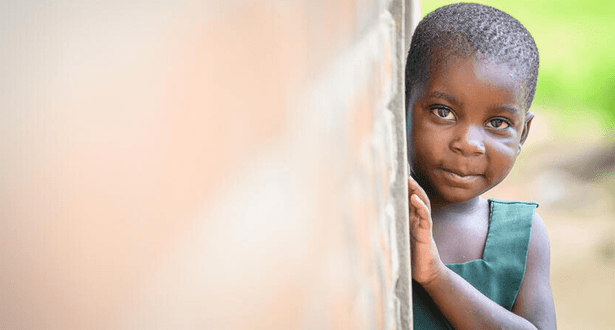 Little girl peers around a corner at her home in Mbonechera ADP, Malawi.