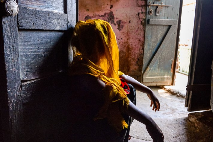 A girl looks away from the camera, her face covered in shadow as they recount her traumatic child marriage