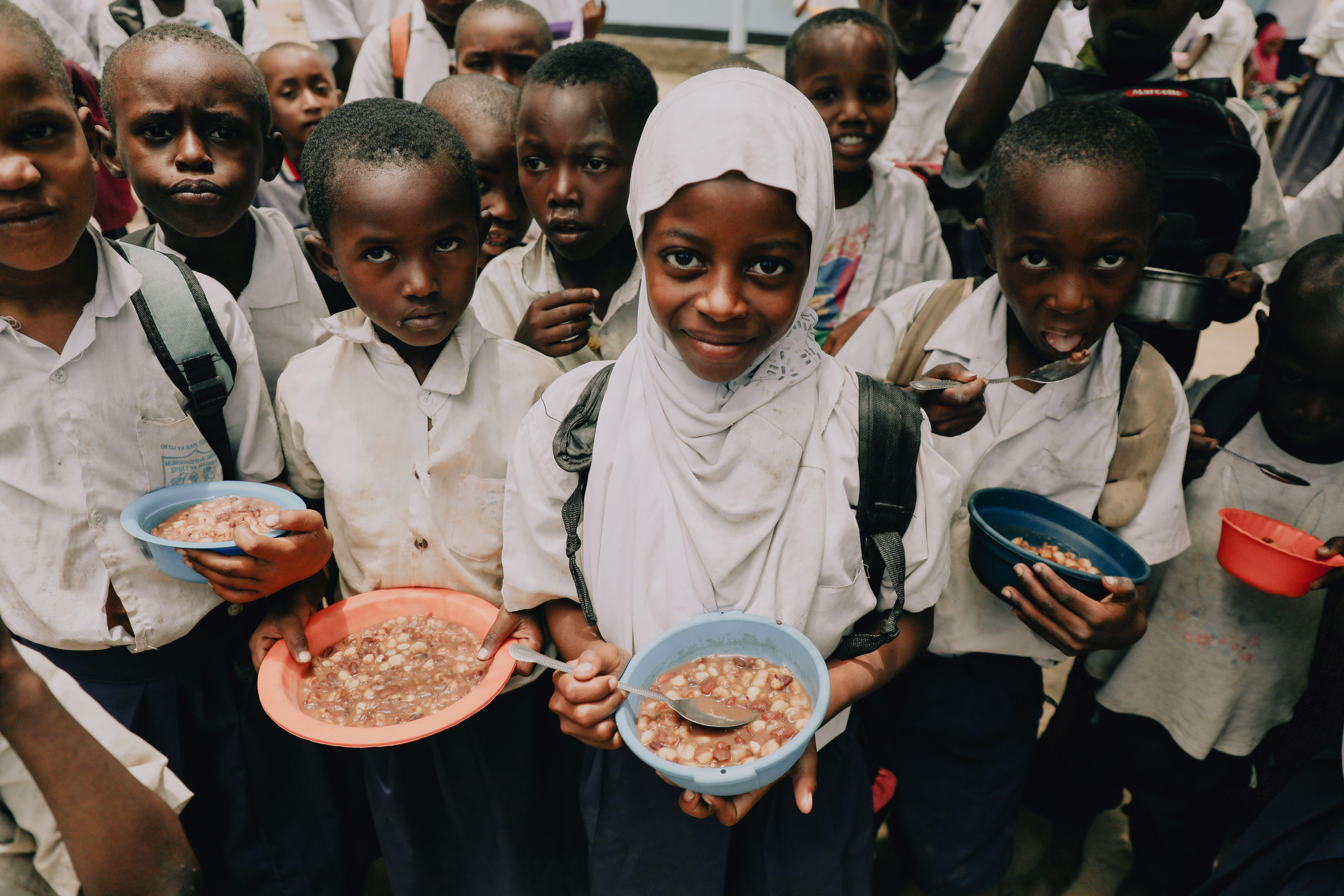 In Tanzania, 9-year-old Rukia (white hijab) holds a plate of food in front of the camera, while her classmates do the same.