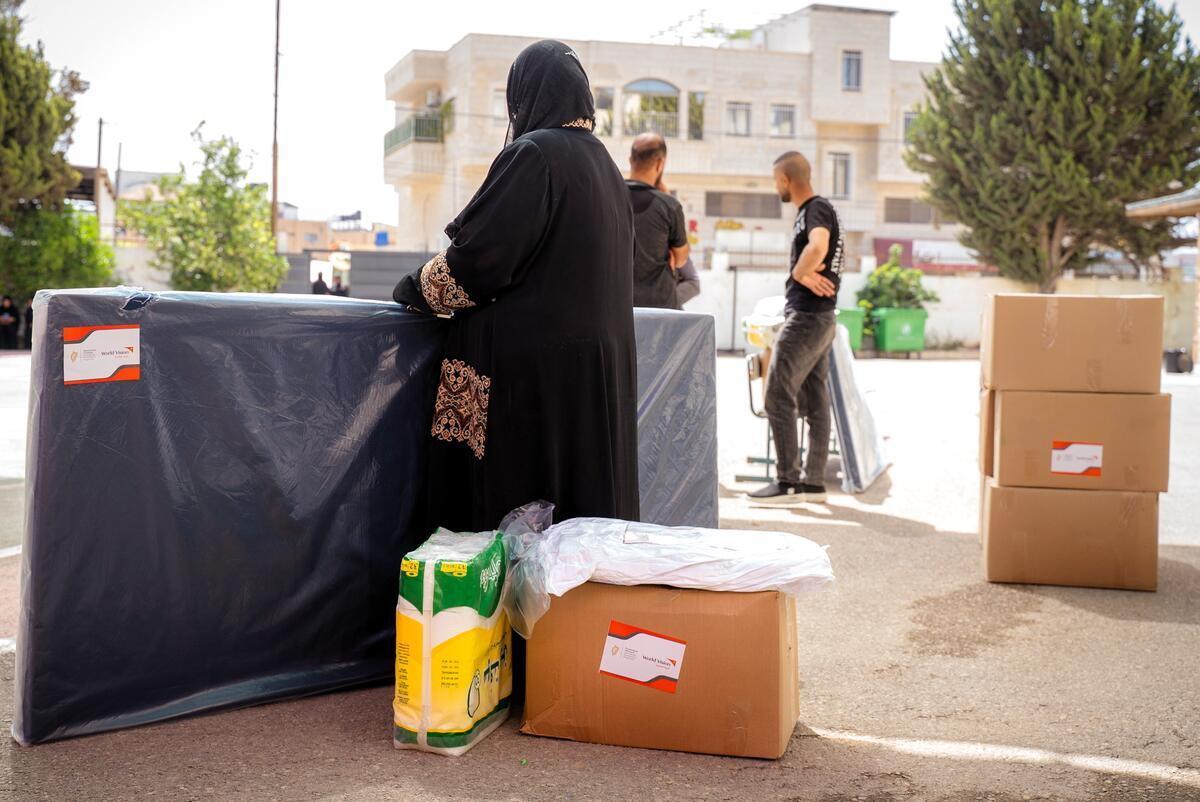 A Palestinian woman is receiving a mattress and other essential items following her forced displacement in the north of the West Bank