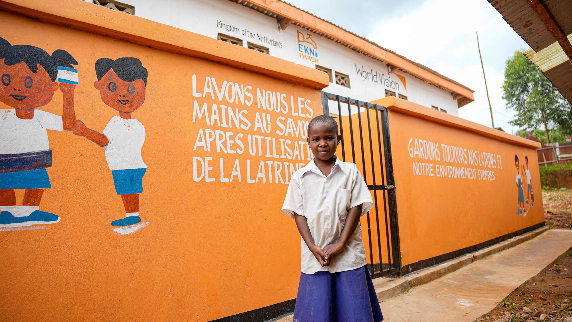 Iragi, 9, poses in front of the toilets built at his school in the DRC
