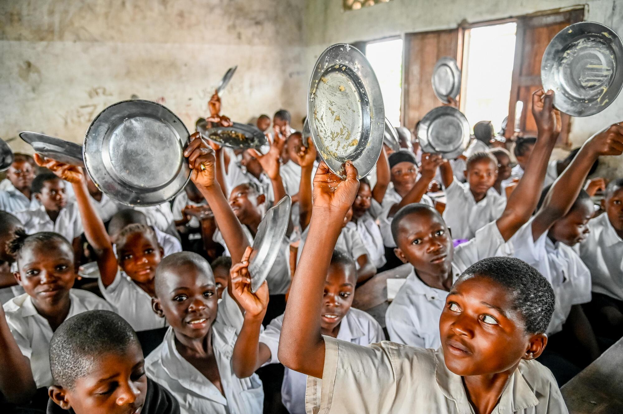 Children raise their plates after finishing their meals during the launch of the Supplementary School Meal Programme in Tanganyika Province, Democratic Republic of the Congo (DRC).
