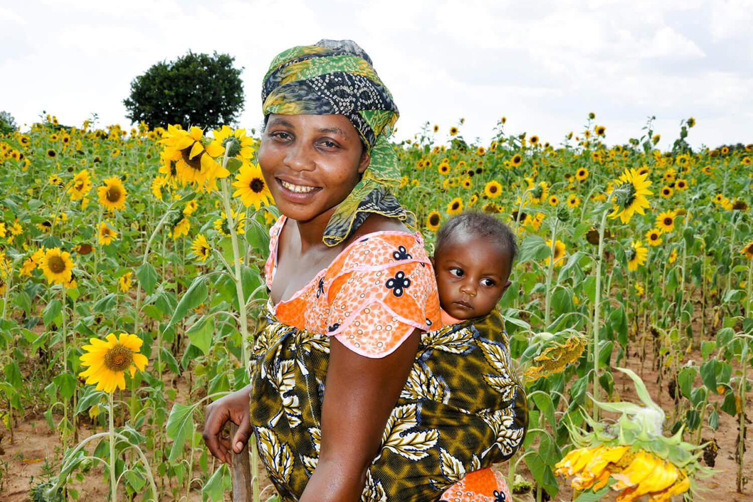 Gladness Samwel, 34, with her 8-month-old son Junior Joseph Njole while clearing her sunflower farm. World Vision supported her family with improved seeds and a machine to produce oil