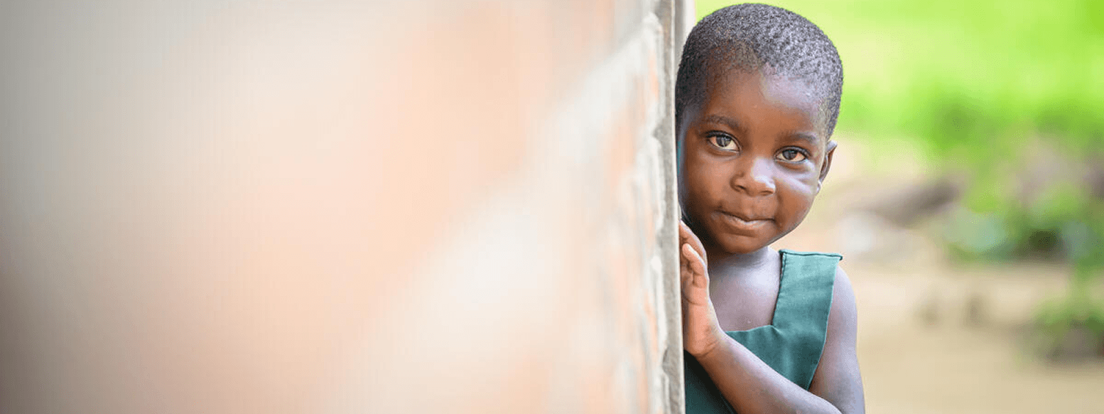 Little girl peers around a corner at her home in Mbonechera ADP, Malawi.