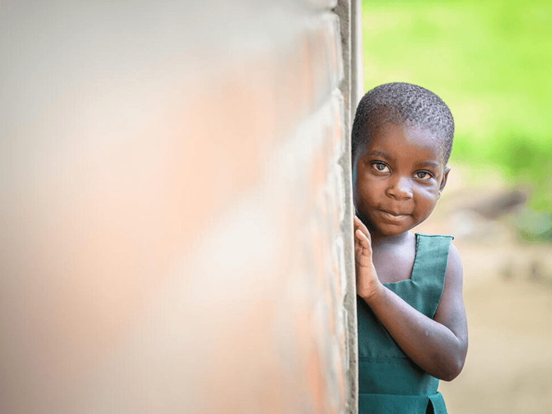 Little girl peers around a corner at her home in Mbonechera ADP, Malawi.